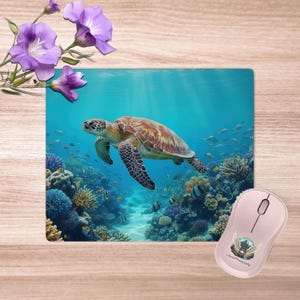 May include: A computer mouse and mouse mat featuring a sea turtle swimming in a coral reef. The mouse is pink with a graphic design. Purple flowers are in the upper left corner. The scene is set underwater.