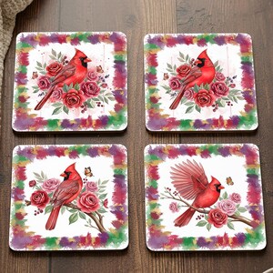 May include: Set of four square coasters featuring a red cardinal bird design. Each coaster has a white background with a watercolor-style border in shades of purple, green, and gold. The cardinal is surrounded by red roses and butterflies.