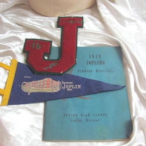 May include: A red felt letter J patch with the number 46, a blue felt pennant with a graphic of a school building and the text Souvenir of Joplin Mo., and a blue 1949 JOPLIMO Student Directory book from Senior High School in Joplin, Missouri.