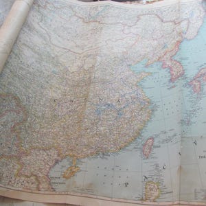 May include: A vintage map of China, printed on a large sheet of paper. The map is rolled up and has a light blue background with brown and yellow lines representing the country's borders and geographical features. The map is titled "China" and includes a legend and scale.