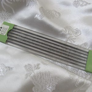 May include: A package of 3B mechanical pencil lead refills. The lead is encased in a clear plastic container with green end caps. The package is resting on a white, floral-patterned fabric.