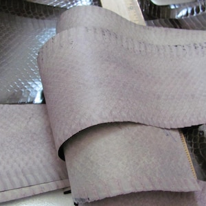May include: A close-up of a piece of gray snakeskin leather. The leather is folded in half and has a textured surface.