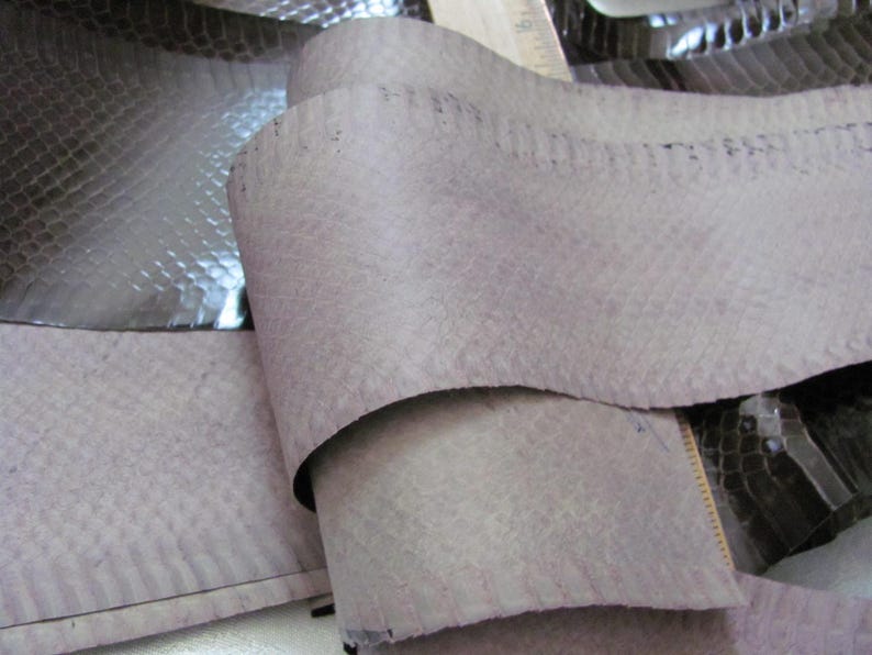 May include: A close-up of a piece of gray snakeskin leather. The leather is folded in half and has a textured surface.