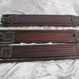 May include: Three antique wooden folding rulers with metal accents. The rulers are a dark reddish-brown color and appear to be made of multiple slats of wood. The metal accents are square and appear to be aged.