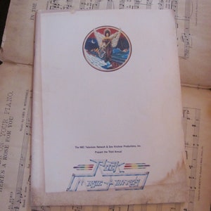 May include: A rectangular program for the Third Annual Rock Music Awards featuring a circular illustration of a winged figure with a guitar. The text reads: The NBC Television Network & Don Kirshner Productions, Inc. Present the Third Annual Rock Music Awards.