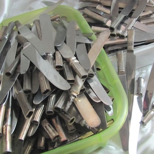 May include: A collection of vintage silver knives with stainless steel blades and ornate handles. The knives are piled in a green plastic container and a white plastic container, suggesting a bulk lot or antique cutlery set.