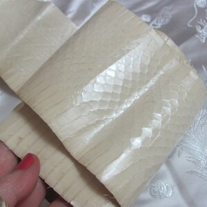 May include: A close-up of a white, textured, snakeskin-like material. The material is folded in half and has a slight sheen.