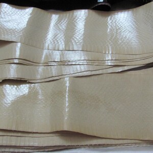 May include: A stack of beige leather strips with a textured surface. The leather has a subtle sheen and appears to be smooth and supple.