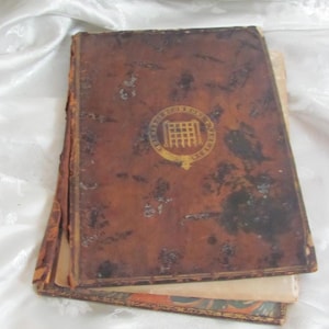May include: A vintage, brown leather-bound book with gold accents and a crest on the front cover. The crest features a building with a gate and the text "The Scottish Society of Antiquaries".