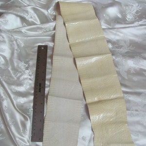 May include: Two strips of off-white leather, one with a smooth surface and the other with a textured surface, are laid out on a white fabric background. A ruler is placed next to the strips of leather.