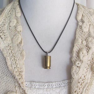 May include: A simple black cord necklace with a gold-colored bullet casing pendant.
