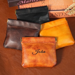 May include: A collection of leather coin purses in various colors: black, brown, and orange. One purse is personalized with the name "John" in cursive script. Each pouch has a metal clasp closure.