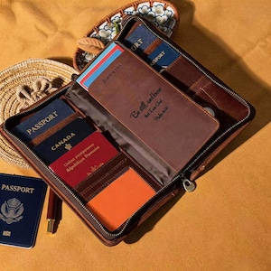 Puede incluir: Un tarjetero de pasaporte de cuero marrón con cremallera, abierto para revelar múltiples pasaportes, tarjetas de embarque y tarjetas. La cubierta tiene el texto "Be still and know that I am God, Psalm 46:10".