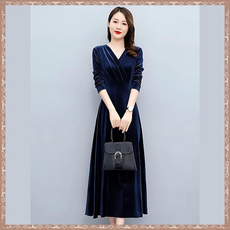 May include: A long, navy blue velvet dress with a V-neck and long sleeves. The dress is paired with a small black handbag. The woman is wearing a watch on her left wrist.