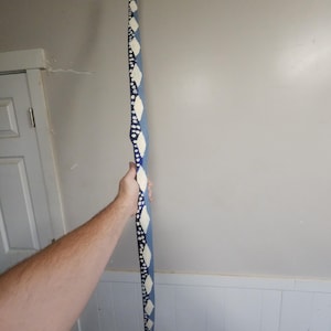 May include: A long, slender, wooden staff painted in shades of blue and white. The staff features a repeating pattern of white diamond shapes and dots against a blue background. The staff is held by a person.