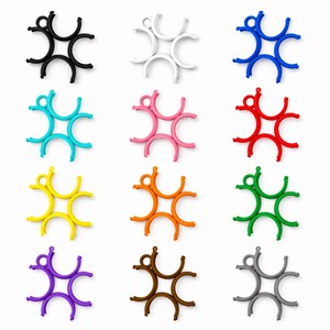 May include: A selection of star-shaped silicone trivets in a range of colours: black, white, blue, turquoise, pink, red, yellow, orange, green, purple, brown, and grey. Each trivet has a central ring and six curved arms.