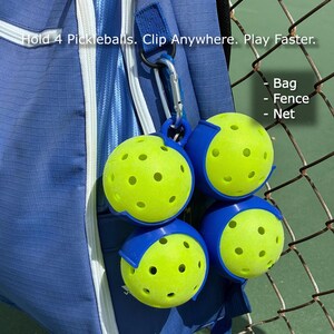 May include: A blue backpack with a silver carabiner clip holding four pickleballs. The pickleballs are yellow with blue holders. Text on the image reads: "Hold 4 Pickleballs. Clip Anywhere. Play Faster."