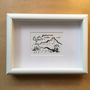 May include: A black and white line drawing of a landscape with a hill, clouds, and plants. The drawing is framed in a white frame.