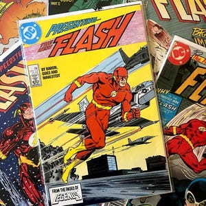 Può includere: Una collezione di fumetti vintage DC Comics con Flash e Wonder Woman. La copertina del fumetto di Flash mostra il supereroe in tuta rossa e gialla che corre davanti a un jet. Sono visibili altri fumetti.