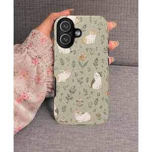 Könnte beinhalten: Eine Handyhülle mit einem sich wiederholenden Muster aus Cartoon-Katzen und floralen Elementen auf hellgrünem Hintergrund. Die Katzen sind in verschiedenen Posen, mit weißem und braunem Fell. Die Hülle hat einen Kameraausschnitt.