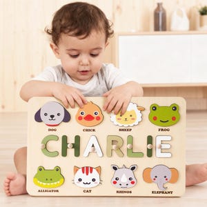 Könnte beinhalten: Holzpuzzle mit Tierformen und dem Namen "CHARLIE" in grünen Buchstaben. Das Puzzle enthält einen Hund, ein Küken, ein Schaf, einen Frosch, einen Alligator, eine Katze, Nashörner und einen Elefanten. Ein Lernspielzeug für Kinder.