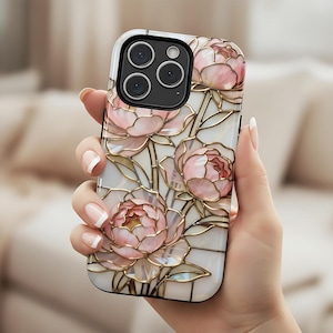 May include: A white and black phone case with a floral design of pink peony flowers. The case has a glossy finish and gold-coloured outlines. The phone case has a camera module with three lenses.