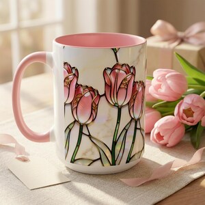 K&ouml;nnte beinhalten: Wei&szlig;er Keramikbecher mit rosa Innenraum und Griff. Der Becher zeigt ein Buntglas-Design aus rosa Tulpen mit goldenen Akzenten. Der Becher ist mit einem Blumendesign verziert und ist ein perfektes Geschenk f&uuml;r jeden Anlass.