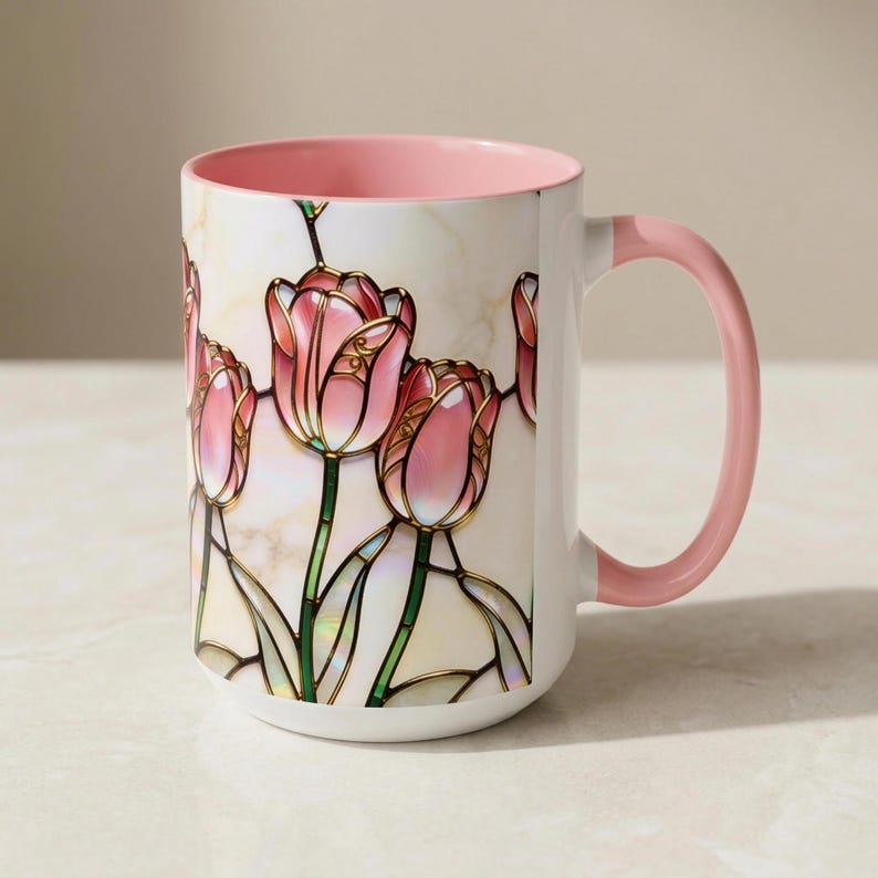 K&ouml;nnte beinhalten: Wei&szlig;e Keramiktasse mit rosa Innenraum und Henkel. Die Tasse zeigt ein Design im Glasmalerei-Stil mit rosa Tulpen mit gr&uuml;nen Stielen und Bl&auml;ttern. Das Design ist vor einem cremefarbenen Hintergrund.