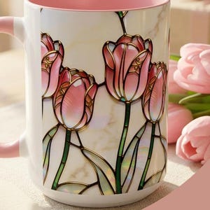 K&ouml;nnte beinhalten: Wei&szlig;e Keramiktasse mit rosa Innenraum und Henkel, mit einem Tulpendesign im Glasmalerei-Stil. Die Tasse tr&auml;gt den Text "A Cup of Beauty" und ist f&uuml;r Hei&szlig;getr&auml;nke geeignet.