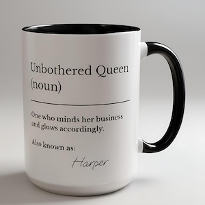 Könnte beinhalten: Weißer Keramikbecher mit schwarzem Innenraum und Henkel. Der Becher zeigt den Text "Unbothered Queen (Substantiv)" mit einer Definition und dem Namen "Harper" in Schrift. Ein stilvoller und funktionaler Artikel für Getränke.