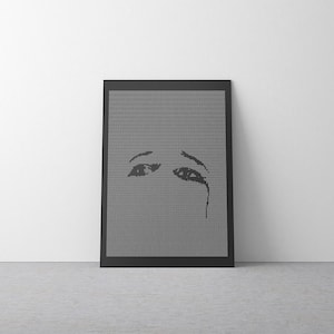 Puede incluir: Una impresión artística enmarcada que presenta una imagen en escala de grises de unos ojos con una lágrima. La obra de arte está compuesta por pequeños puntos, creando un efecto texturizado. El marco negro contrasta con la pared blanca.