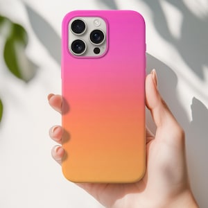 Könnte beinhalten: Eine lebendige, farbverlaufende Handyhülle in Pink-, Orange- und Gelbtönen. Die Hülle hat eine glatte Oberfläche und ist für ein Smartphone mit mehreren Kameralinsen konzipiert. Die Hülle wird in einer Hand vor weißem Hintergrund gehalten.