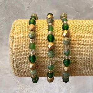 May include: Three beaded bracelets featuring alternating round green glass beads and metallic gold-toned beads. Each bracelet is constructed with a repeating pattern of translucent emerald green spheres and textured gold-colored spherical accents.