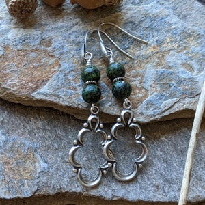 May include: A pair of silver earrings with green stone beads. The earrings feature a delicate, ornate design with a floral motif.