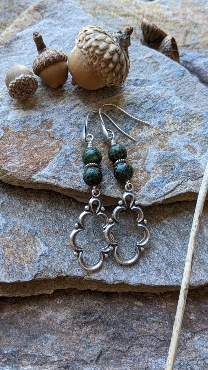 May include: A pair of silver earrings with green stone beads. The earrings feature a delicate, ornate design with a floral motif.