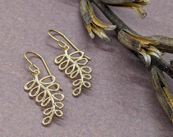 May include: A pair of gold leaf-shaped dangle earrings. The earrings are made of a delicate, intricate design and hang from a simple hook.