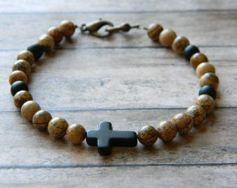 May include: A brown and black beaded bracelet with a black cross charm. The bracelet is made with natural stones and has a simple, elegant design.