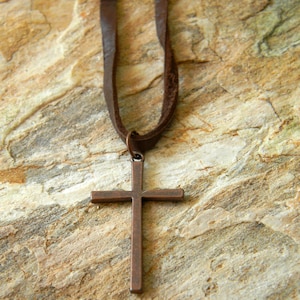 May include: A brown leather cord necklace with a simple copper cross pendant.