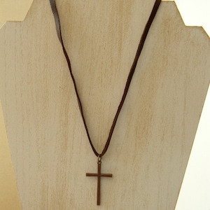 May include: A brown leather cord necklace with a simple brown metal cross pendant.