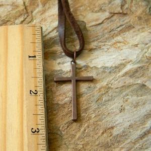 May include: A brown leather cord necklace with a copper cross pendant. The cross is about 2 inches tall.