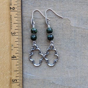May include: Silver dangle earrings with green speckled beads and a decorative filigree design.