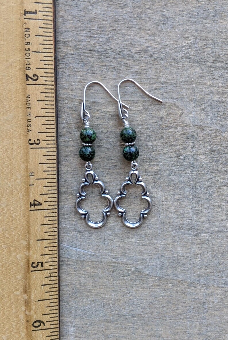 May include: Silver dangle earrings with green speckled beads and a decorative filigree design.