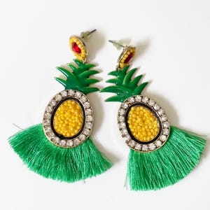 May include: A pair of green pineapple earrings with yellow and white beading and a green tassel.