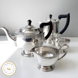 Peut inclure: Un service à thé en argent avec des poignées noires. L'ensemble comprend une théière, un pot à crème, un sucrier et un plateau assorti. L'ensemble est décoré d'un motif floral.