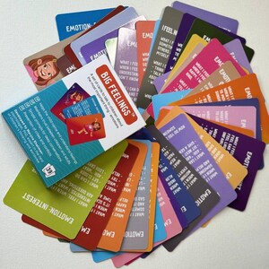 May include: A set of colorful Big Feelings cards for children, featuring illustrations and prompts about emotions. The cards are fanned out, with the box visible, displaying the title and purpose of the cards.