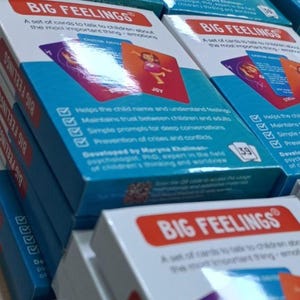 May include: Stacks of "Big Feelings" card sets. Each box features a red and white label with the product name and a blue background with product information. The cards are designed to help children understand emotions.