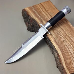 May include: A fixed-blade knife with a silver-toned metal blade featuring a serrated spine and a black wrapped handle. The pommel is textured silver metal. The blade is etched with the text ZH Crafts near the base of the cutting edge.