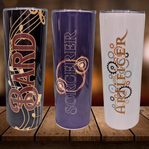 May include: Three insulated tumblers with different designs. One is black with musical notes and the word "BARD". The second is purple with "SORCERER". The third is white with gears and "ARTIFICER".