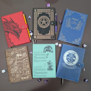 May include: Five rectangular journals with various covers: a red dragon design, a black pentagram motif, a blue book titled My Legendary Adventures, a brown map print, and a blue Role Playing Games Club book, all surrounded by scattered polyhedral dice.