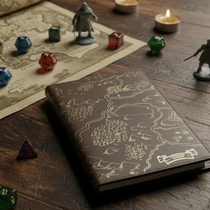 May include: A brown notebook with a gold-stamped map design on the cover, featuring a scroll-shaped label in the corner. The notebook is surrounded by various multi-colored polyhedral dice, two miniature fantasy figurines, and a large paper map.